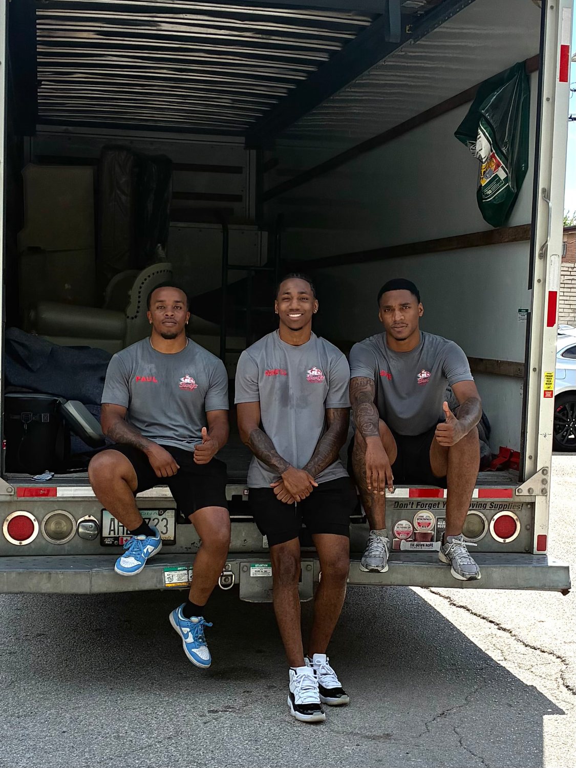 Three Swift Movers crew members in grey uniforms sitting on the tail of a loaded moving truck