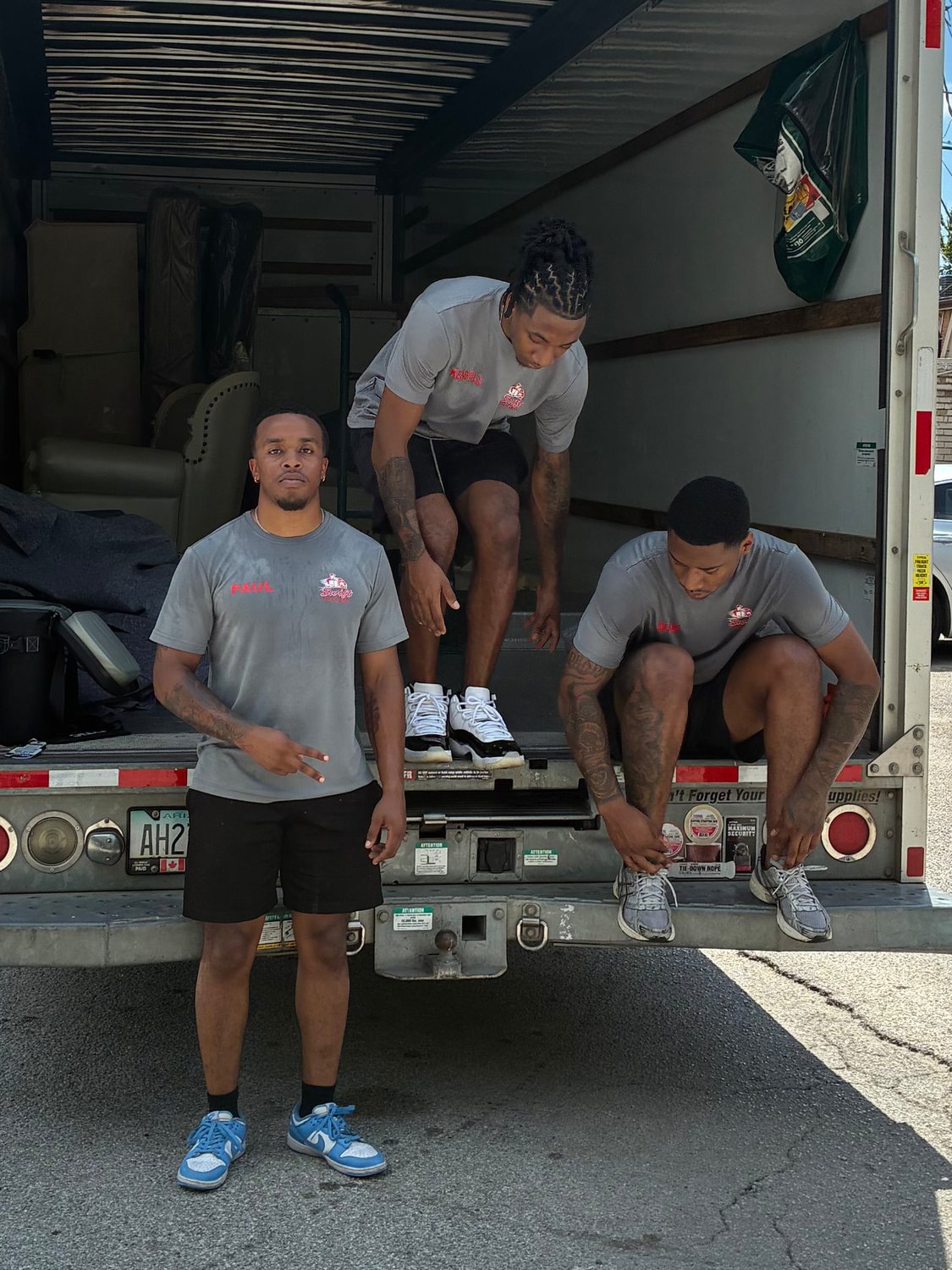 Three crew members in matching grey uniforms at the back of a moving truck